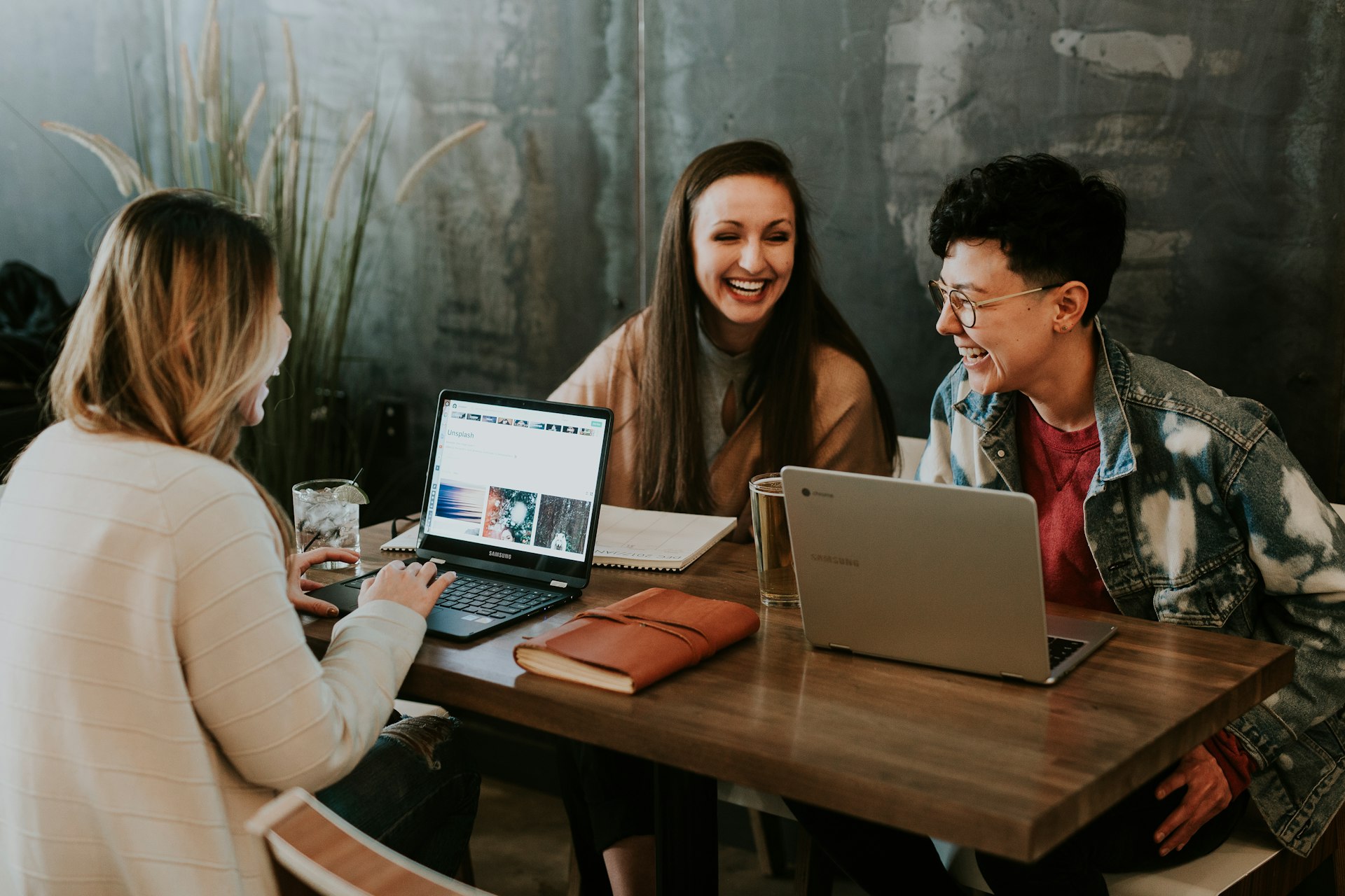 Three colleagues smiling and working together on laptops at a table